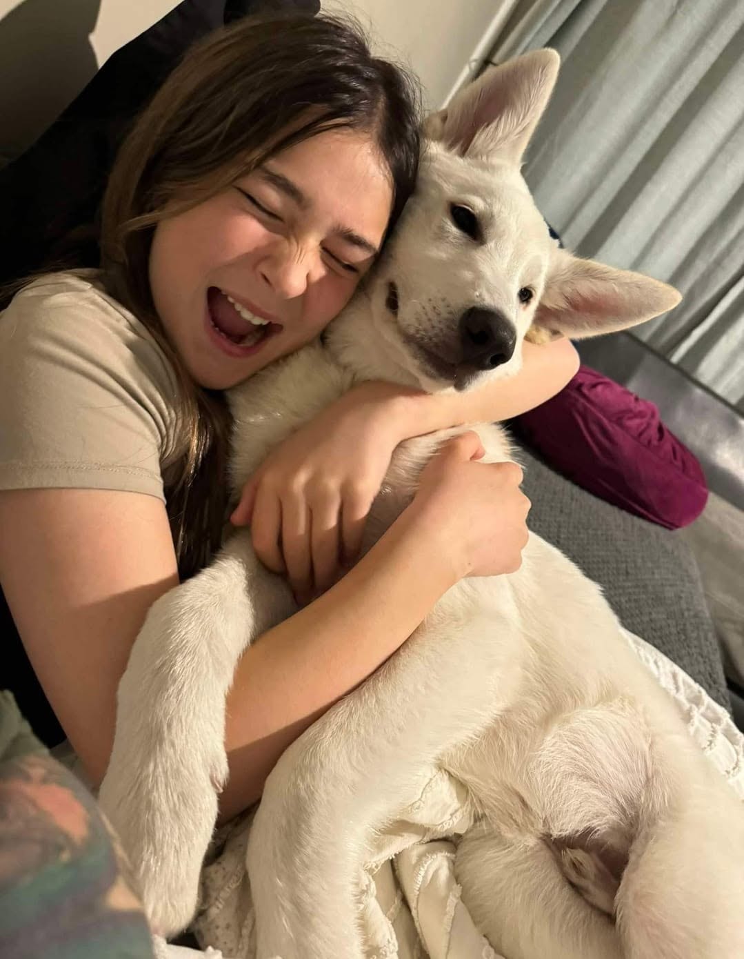A young woman laughing and hugging a white foster puppy